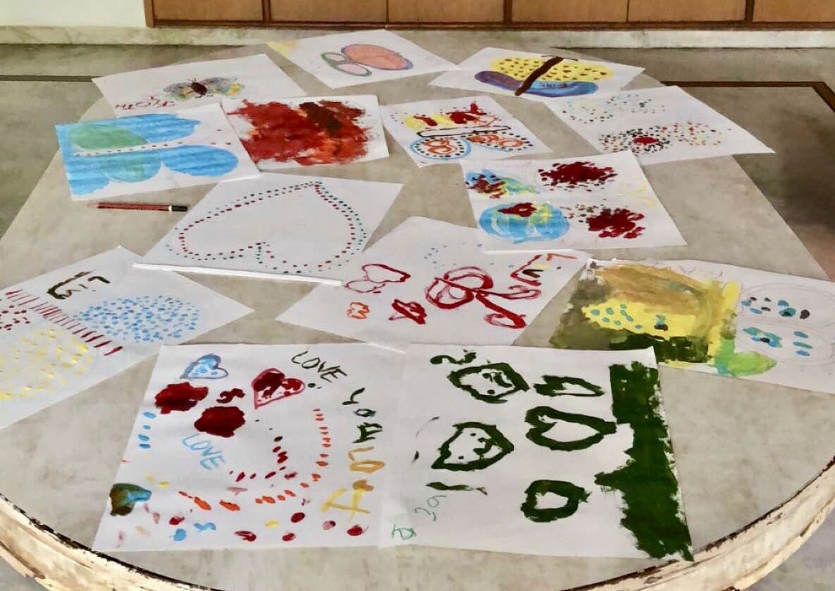 Children's paintings of hearts, butterflies and the word “Love” laid out on a table to dry.