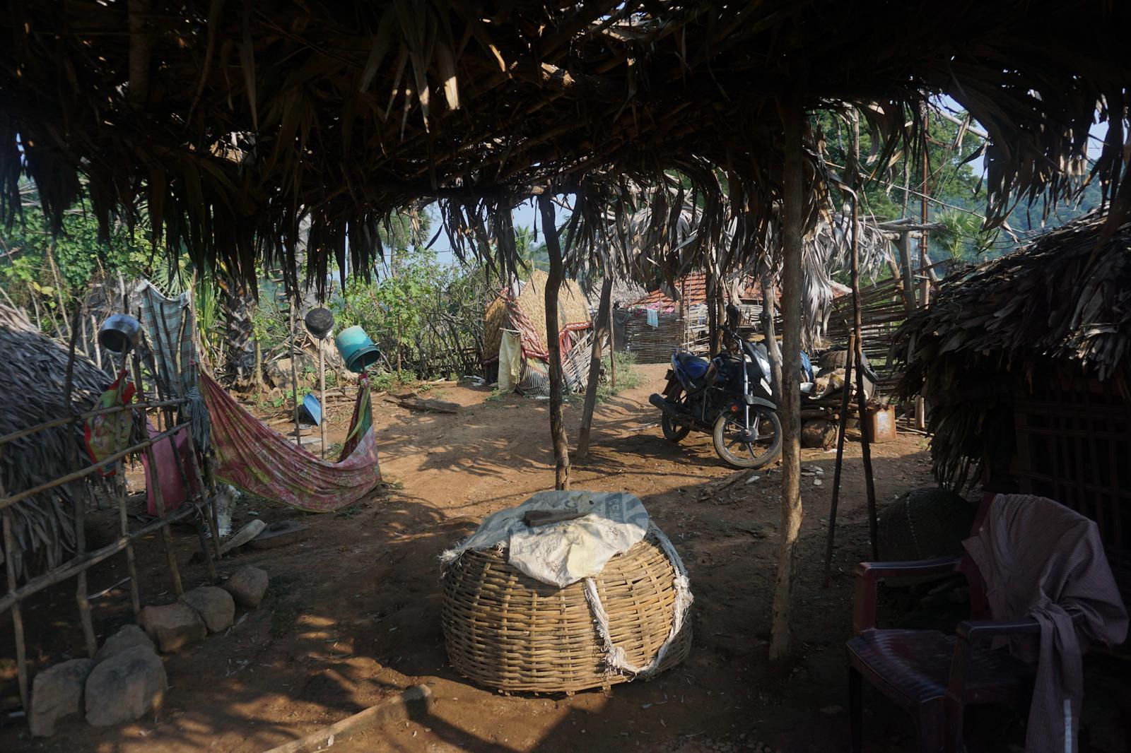 An open shelter with a thatched roof in a village in India, with a hammock and a woven basket underneath.